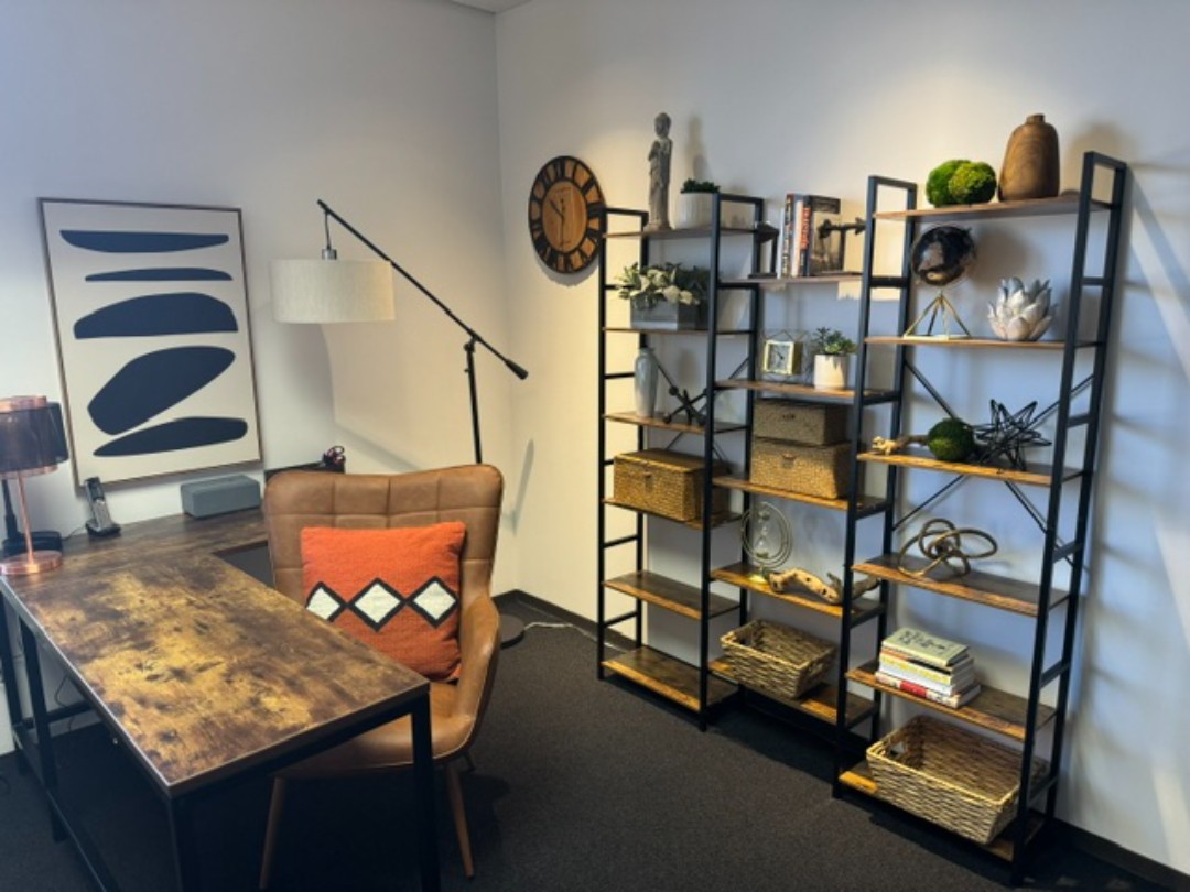 A bookshelf with many baskets and trinkets on it. A desk with chair is against the other wall